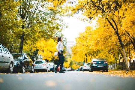 Photo for Girl Walking in the Middle of Street in Fall Season - Royalty Free Image