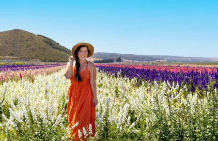Foto de Mujer en vestido naranja y sombrero estaba en los campos de flores sonriendo a la cámara - Imagen libre de derechos