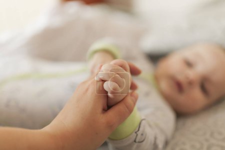 Téléchargez les photos : Bébé bébé couché sur le lit et tenant la main de maman - en image libre de droit