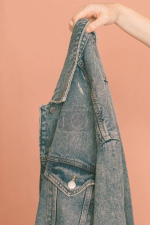 Photo for Hand holding a jean jacket against a pink backdrop - Royalty Free Image