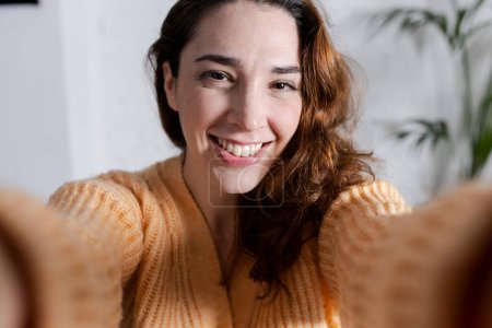 Téléchargez les photos : Sourire belle jeune femme prendre un selfie dans la maison - en image libre de droit