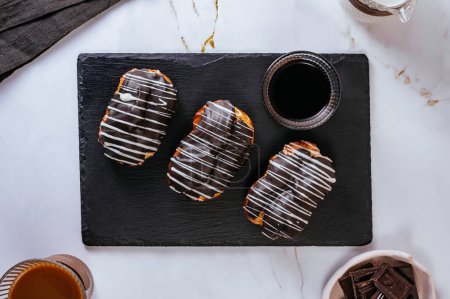 Photo for Homemade eclair in chocolate glaze on a plate. Coffee in a glass - Royalty Free Image