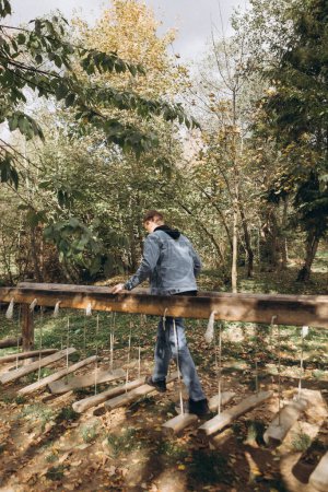 Photo for Man walks on a wooden suspension bridge in the park - Royalty Free Image