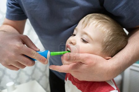 Foto de Papá ayuda a cepillar los dientes de los niños con un cepillo de dientes eléctrico colorido - Imagen libre de derechos