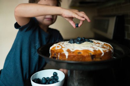 Foto de Chico poniendo los toques finales en un pastel de arándanos - Imagen libre de derechos
