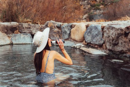 Photo for Portrait of woman in hat drinking beer in natural hot springs - Royalty Free Image