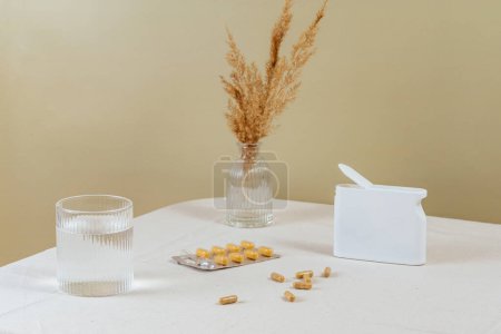 Téléchargez les photos : Vitamines en capsules dispersées sur la table. un verre d'eau. - en image libre de droit