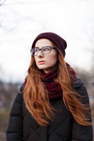 Photo for Red-haired woman in a hat and down jacket in the middle of the park - Royalty Free Image
