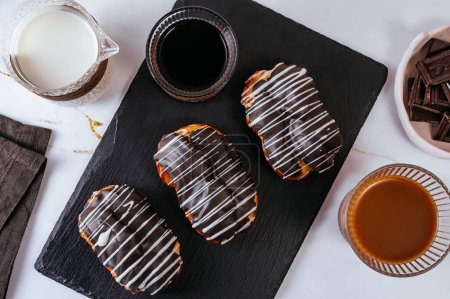 Photo for Homemade eclair in chocolate glaze on a plate. Coffee in a glass - Royalty Free Image