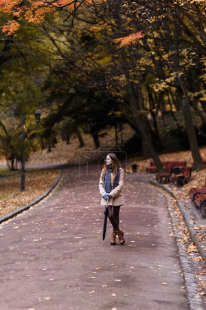 Foto de Mujer en un abrigo y bufanda con un paraguas en las manos en el parque de otoño - Imagen libre de derechos
