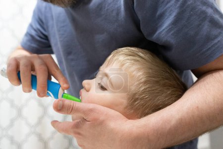 Foto de Primer plano de los dientes de cepillo de hijo que ayudan al padre con cepillo de dientes eléctrico - Imagen libre de derechos