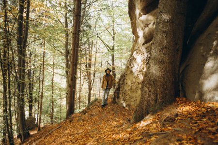 Téléchargez les photos : Femme en veste et chapeau marche dans les bois près des montagnes - en image libre de droit