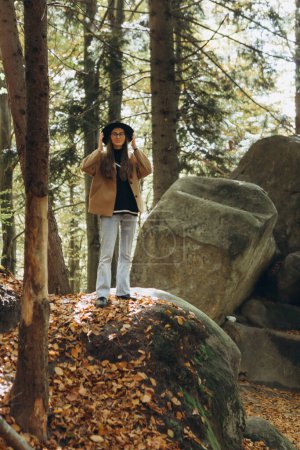 Téléchargez les photos : Jeune femme dans une veste brune et chapeau noir dans la forêt - en image libre de droit