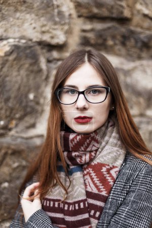 Photo for Young woman in glasses wearing a coat wrapped in a scarf - Royalty Free Image