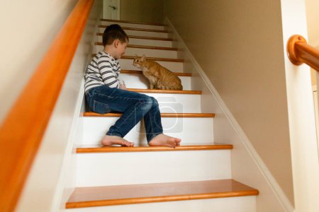 Téléchargez les photos : Orange chat penche et regarde vers garçon assis sur les escaliers - en image libre de droit