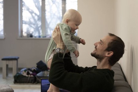 Téléchargez les photos : Papa tient le bébé devant lui dans ses bras et sourit - en image libre de droit