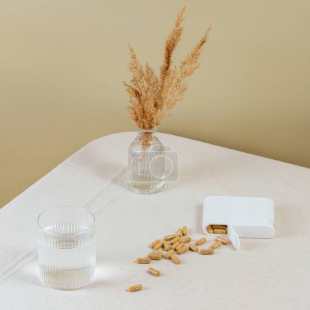Foto de Vitaminas en cápsulas esparcidas sobre la mesa. un vaso de agua. - Imagen libre de derechos