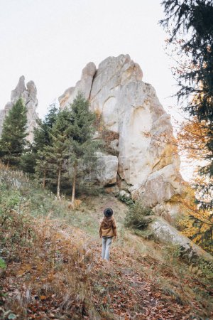 Téléchargez les photos : Femme en veste et chapeau marche dans les bois près des montagnes - en image libre de droit