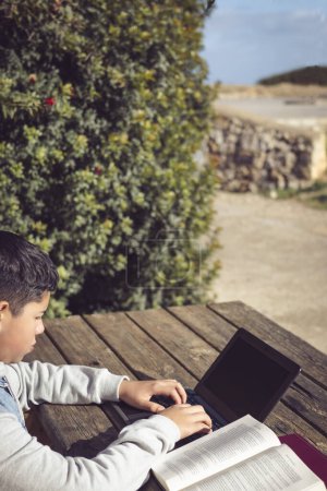 Téléchargez les photos : Jeune étudiant latin, en plein air, en utilisant un ordinateur portable assis dans un parc - en image libre de droit