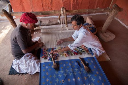 Téléchargez les photos : Dans un village tribal éthique en dehors de Jodhpur, un tisserand travaille à la création d'un tapis traditionnel - en image libre de droit
