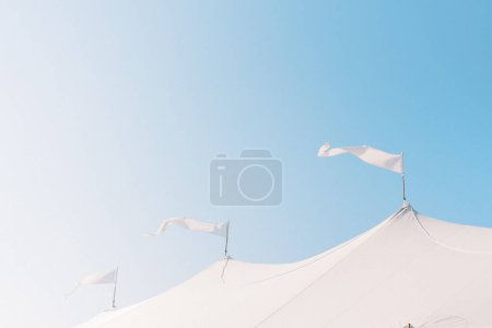 Téléchargez les photos : Trois drapeaux blancs flottant en brise sur le dessus de la tente par une journée ensoleillée - en image libre de droit
