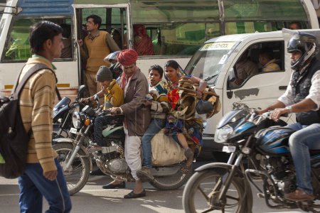 Téléchargez les photos : Quatre membres d'une famille indienne s'entassent sur une moto au milieu d'un embouteillage urbain - en image libre de droit