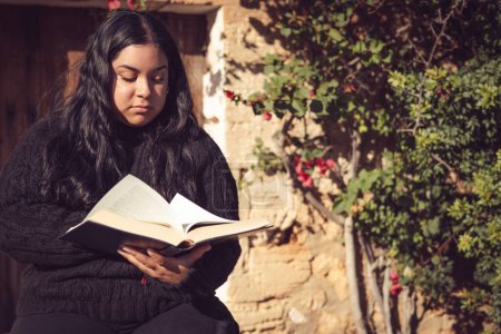 Téléchargez les photos : Jeune femme latine assise à lire un livre - en image libre de droit