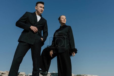 Téléchargez les photos : Un homme et une fille en vêtements noirs se dressent contre un ciel bleu sans nuages - en image libre de droit