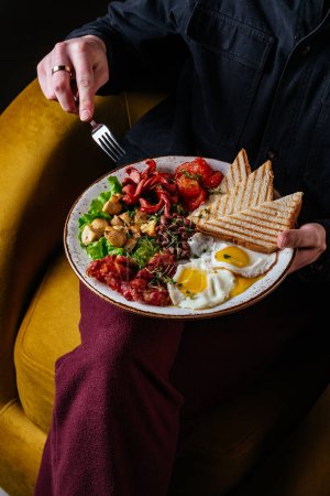 Photo for A man has an English breakfast with scrambled eggs, bacon, beans, mushrooms - Royalty Free Image