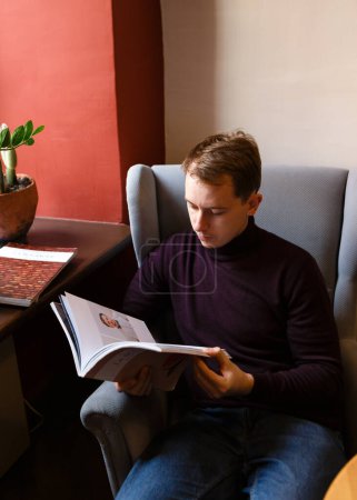 Téléchargez les photos : Jeune homme assis seul à une table avec des magazines - en image libre de droit