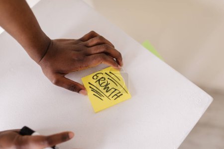 Photo for Black person writing growth on a sticky note on white work desk - Royalty Free Image