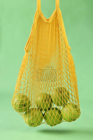 Téléchargez les photos : Concept zéro déchet. Pommes vertes dans un sac réutilisable en maille jaune sur fond vert - en image libre de droit