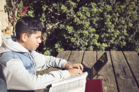 Téléchargez les photos : Jeune étudiant latin écrit sur ordinateur portable, en plein air - en image libre de droit