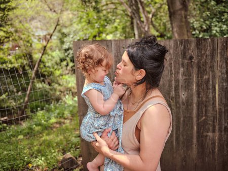 Téléchargez les photos : Maman et fille embrasser et montrer de l'affection dans clôturé dans la cour arrière - en image libre de droit