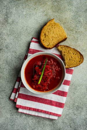 Téléchargez les photos : Red beetroot borscht served in bowl with bread pieces on red and white stripped towel - en image libre de droit
