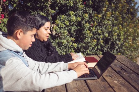 Téléchargez les photos : Deux jeunes étudiants latino, en plein air, utilisant des ordinateurs portables, assis dans un parc - en image libre de droit