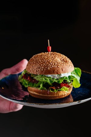 Foto de Hamburguesa jugosa en un plato sobre un fondo oscuro - Imagen libre de derechos