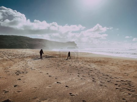 Téléchargez les photos : Personnes silhouettes sombres sur une large plage avec des falaises à Nazare - en image libre de droit