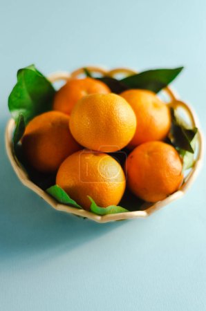 Téléchargez les photos : Mandarines dans un panier sur fond bleu - en image libre de droit