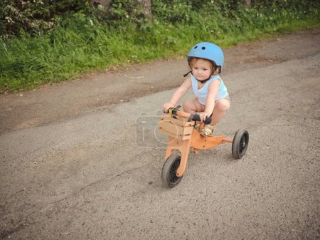 Foto de Niño en camiseta azul monta un triciclo de madera - Imagen libre de derechos
