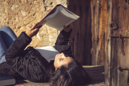 Foto de Mujer latina acostada, leyendo un libro en el jardín - Imagen libre de derechos