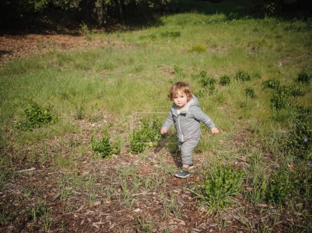 Photo for One year old female in grey snow suit playing in grassy field - Royalty Free Image