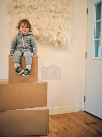 Photo for One year old sits on three cardboard boxes in family home - Royalty Free Image