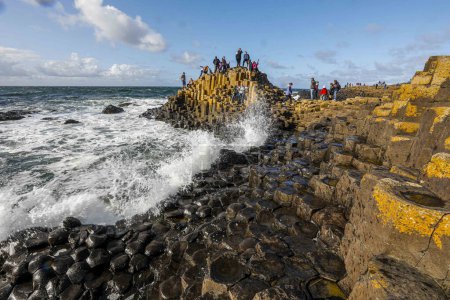 Téléchargez les photos : People hike along the Giant's Causeway an area of about 40,000 interlocking basalt columns, the result of an ancient volcanic fissure eruption. It is located in County Antrim on the north coast of Northern Ireland. t was declared a World Heritage Sit - en image libre de droit