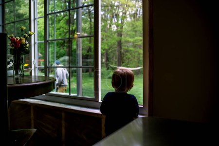 Foto de Hijo pequeño mirando al padre curiosamente desde la ventana en verano - Imagen libre de derechos
