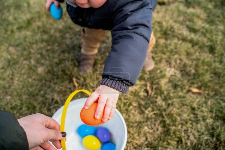 Téléchargez les photos : Bébé Garçon Placer Oeuf de Pâques coloré dans un seau en plastique - en image libre de droit