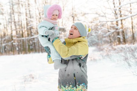 Téléchargez les photos : Père et fille d'un an tout-petit marchent dans un parc enneigé - en image libre de droit