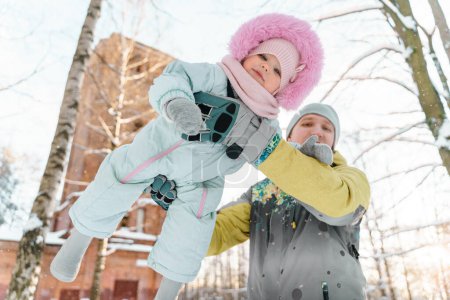 Téléchargez les photos : Père et fille d'un an tout-petit marchent dans un parc enneigé - en image libre de droit