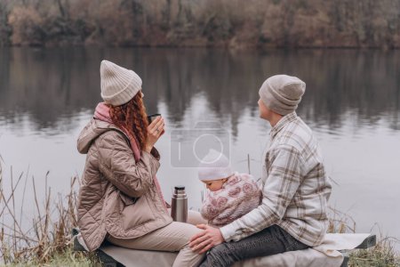 Foto de Padres y una niña se relajan en un parque de primavera cerca del río - Imagen libre de derechos