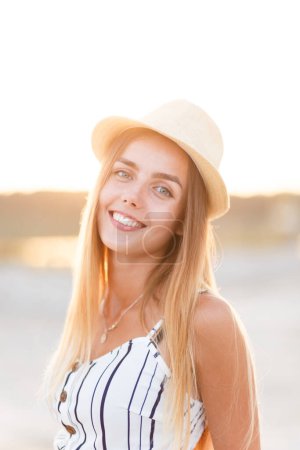 Téléchargez les photos : Young blonde in a hat and summer dress on the beach - en image libre de droit